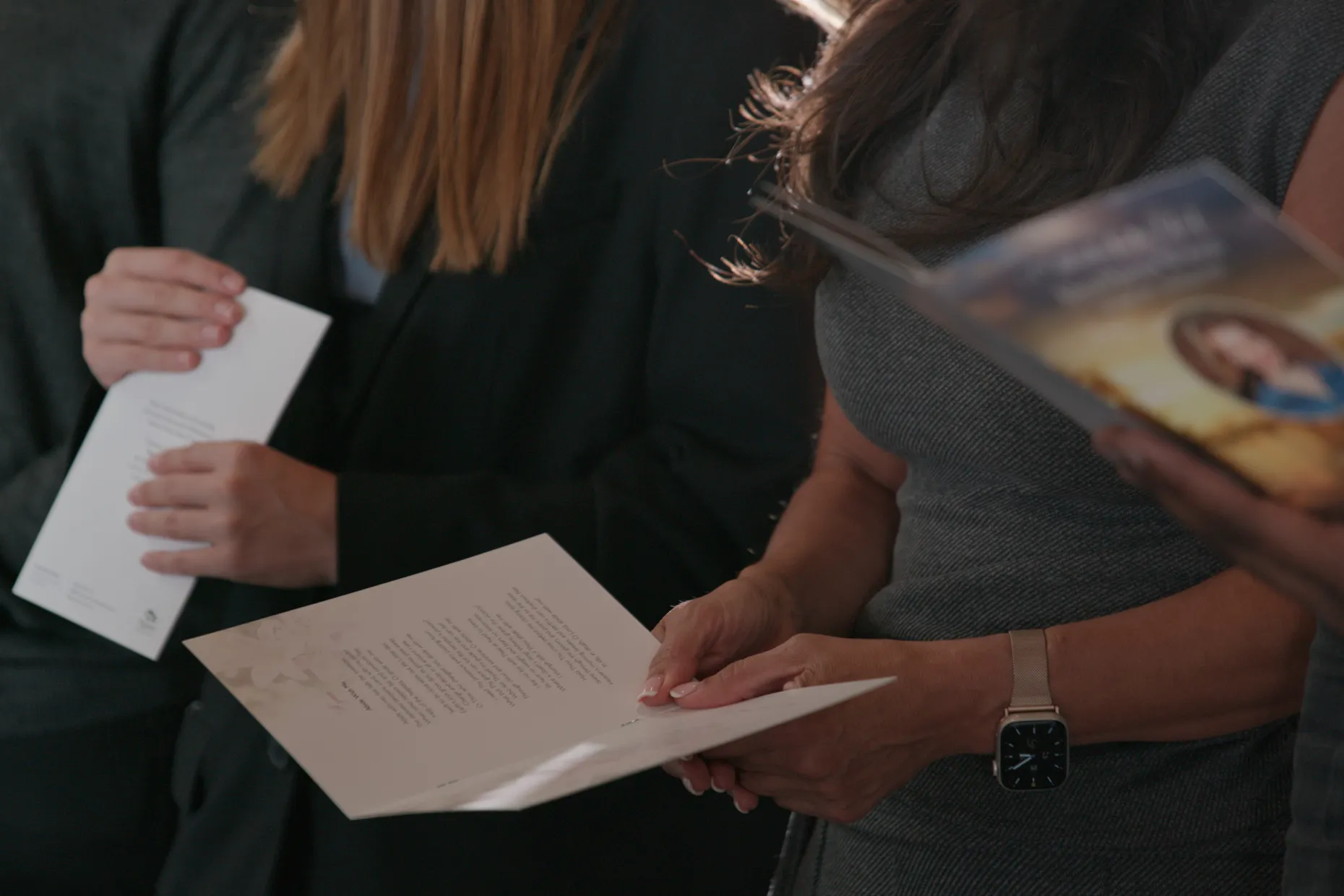 Mourners in dark clothing holding printed orders of service at a funeral.