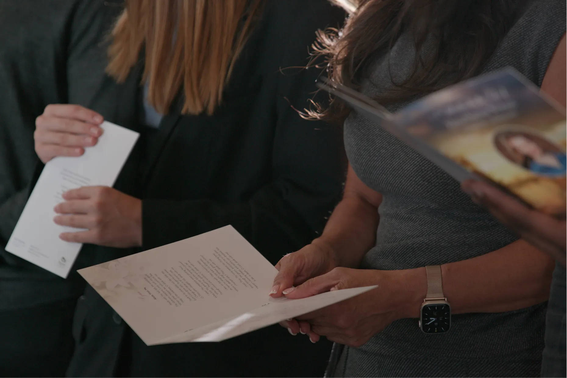 Close-up of mourners holding printed orders of service at a funeral service.