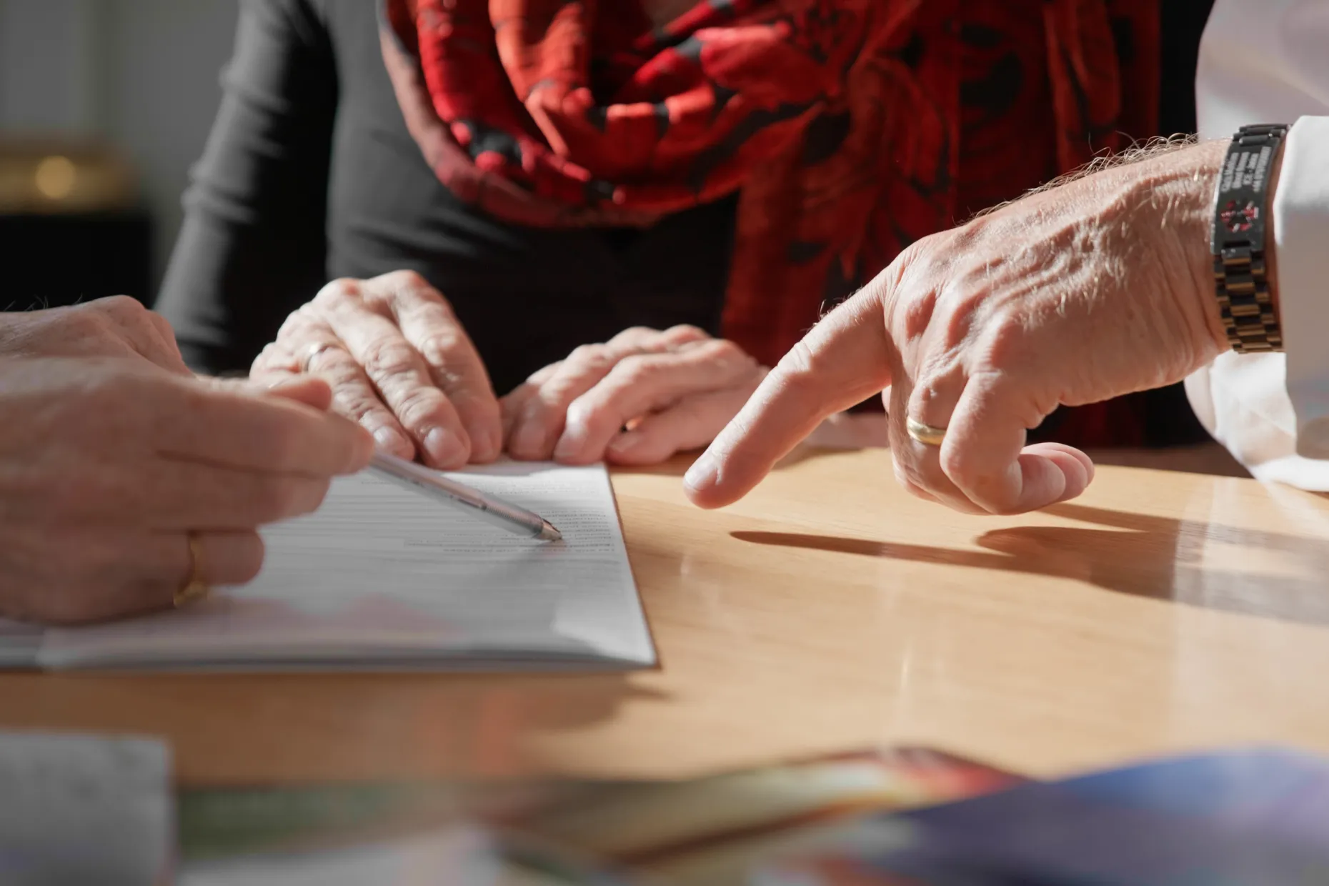 Close-up of hands signing a document at a table while another person points at it.